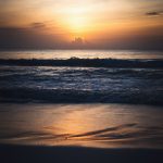 the sun is setting over the ocean on the beach