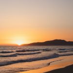 the sun is setting over the ocean on the beach